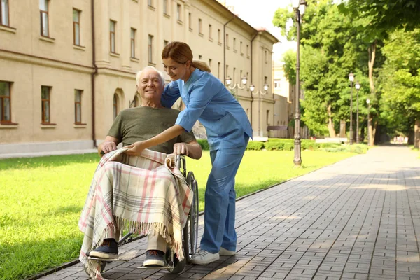 Ευτυχισμένος νοσοκόμα βοηθώντας τον ηλικιωμένο άνθρωπο σε αναπηρικό αμαξίδιο στο πάρκο — Φωτογραφία Αρχείου