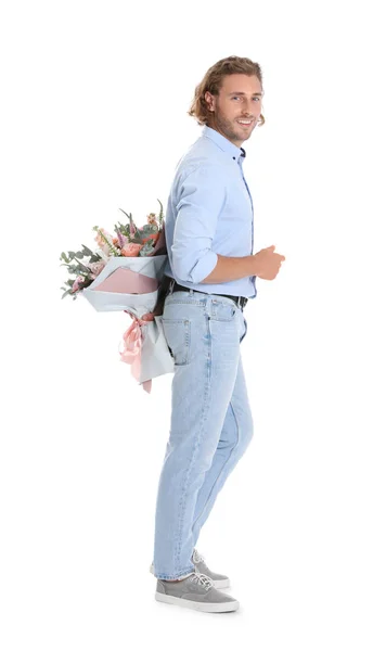 Joven hombre guapo escondiendo hermoso ramo de flores detrás de su espalda sobre fondo blanco — Foto de Stock