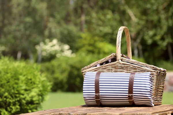 Panier pique-nique avec couverture sur table en bois dans le jardin. Espace pour le texte — Photo