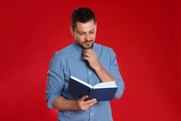 Hombre guapo leyendo libro sobre fondo rojo — Foto de Stock