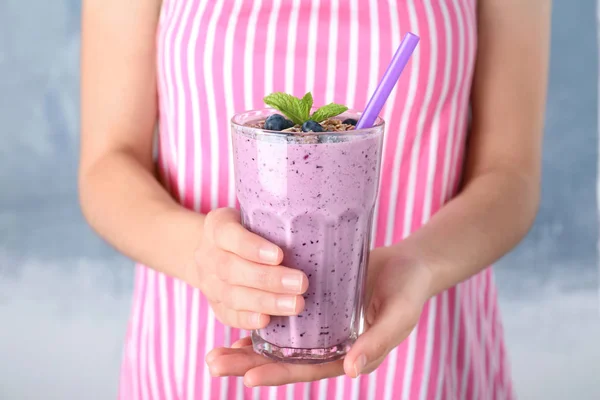 Mujer sosteniendo vaso de delicioso batido de arándanos sobre fondo azul, primer plano — Foto de Stock