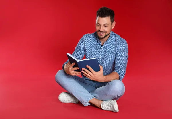 Yakışıklı adam kırmızı arka plan üzerinde kitap okuma — Stok fotoğraf