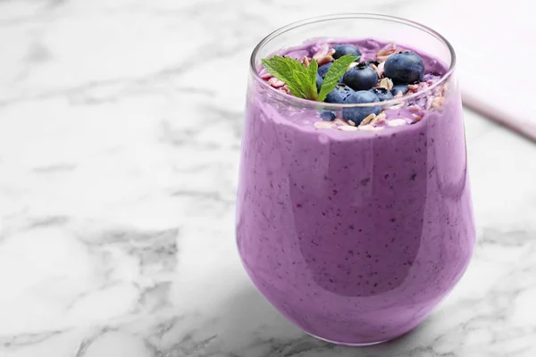 Glass of delicious blueberry smoothie with granola and mint on white marble table. Space for text — Stock Photo, Image