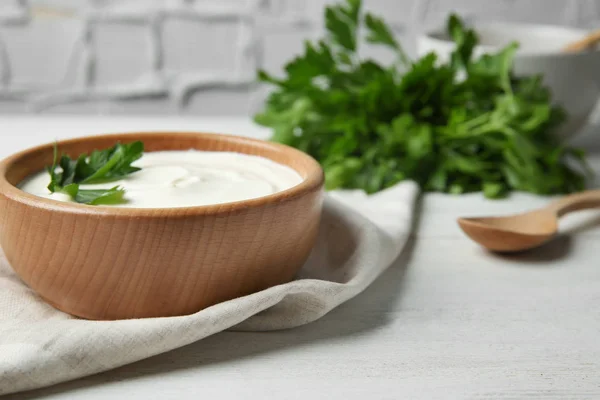 Bowl of fresh sour cream with parsley and wooden spoon on white wooden table. Space for text — Stock Photo, Image