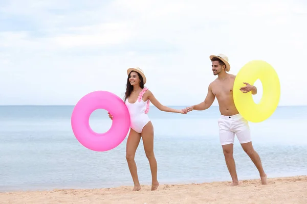 Glückliches junges Paar hat Spaß mit aufblasbaren Ringen am Strand am Meer — Stockfoto