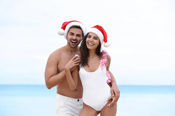 Feliz pareja joven con sombreros de Santa juntos en la playa — Foto de Stock