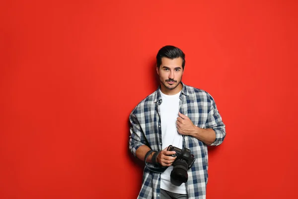 Young photographer with professional camera on red background. Space for text — Stock Photo, Image