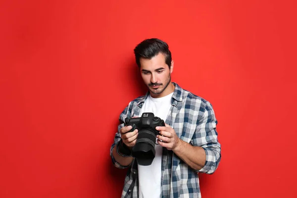 Jovem fotógrafo com câmera profissional em fundo vermelho — Fotografia de Stock