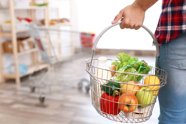 Man met winkelmandje vol met producten in supermarkt, close-up — Stockfoto