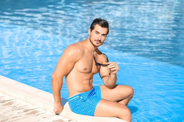 화창한 날에 수영장 가장자리에 앉아 있는 잘 생긴 젊은 남자 — 스톡 사진