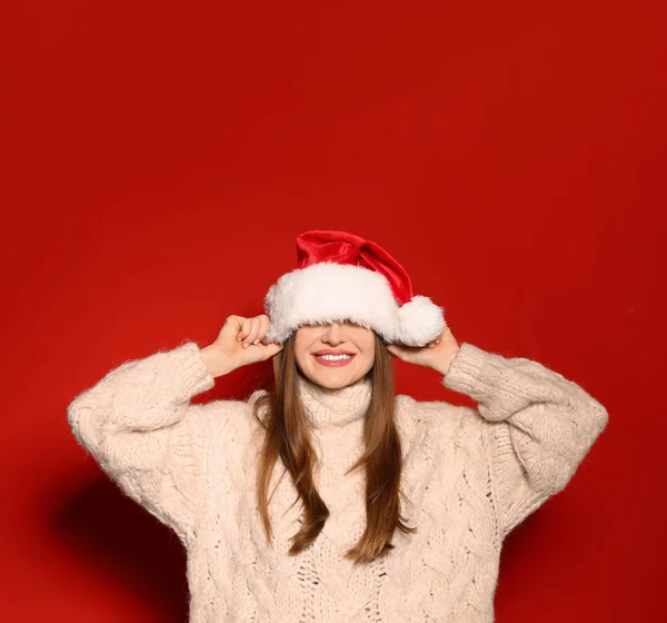 Jeune femme en pull de Noël et chapeau de Père Noël sur fond rouge — Photo
