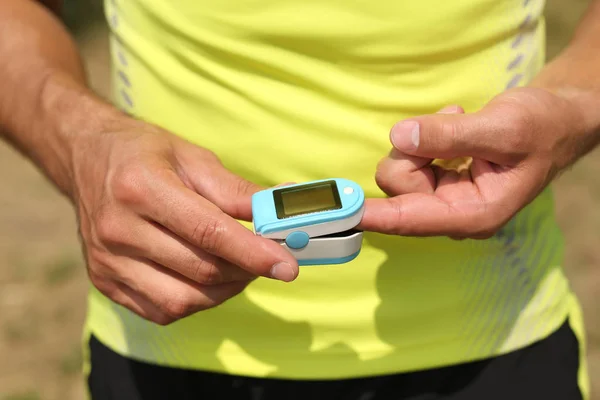 Young man checking pulse with medical device after training outdoors, closeup — Stock Photo, Image