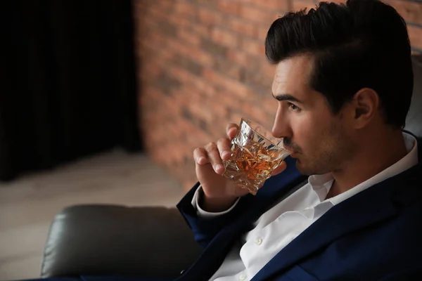 Jeune homme avec un verre de whisky près du mur de briques à l'intérieur. Espace pour le texte — Photo