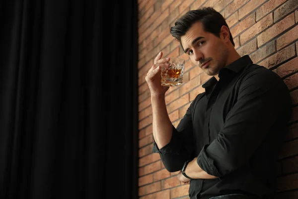 Jeune homme avec un verre de whisky près du mur de briques à l'intérieur. Espace pour le texte — Photo