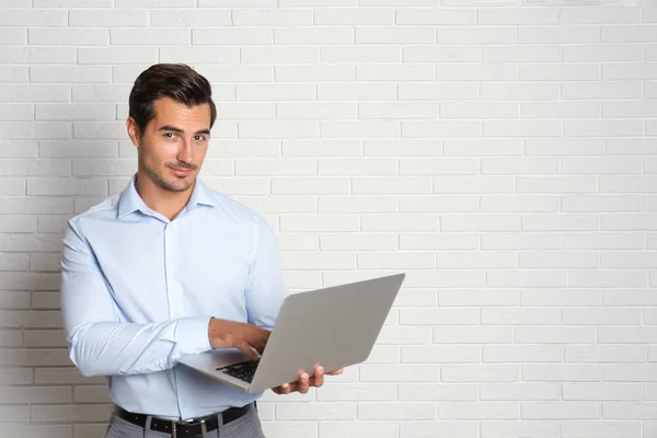 Jovem professor com laptop perto da parede de tijolo. Espaço para texto — Fotografia de Stock