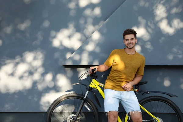 Beau jeune homme avec vélo près du mur gris sur la rue de la ville. Espace pour le texte — Photo