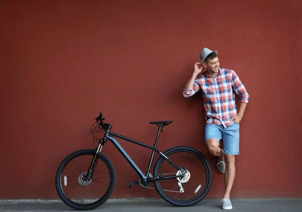 Красивий чоловік з сучасним велосипедом біля червоної стіни на відкритому повітрі — стокове фото