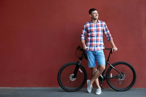 Красивий чоловік з сучасним велосипедом біля червоної стіни на відкритому повітрі — стокове фото