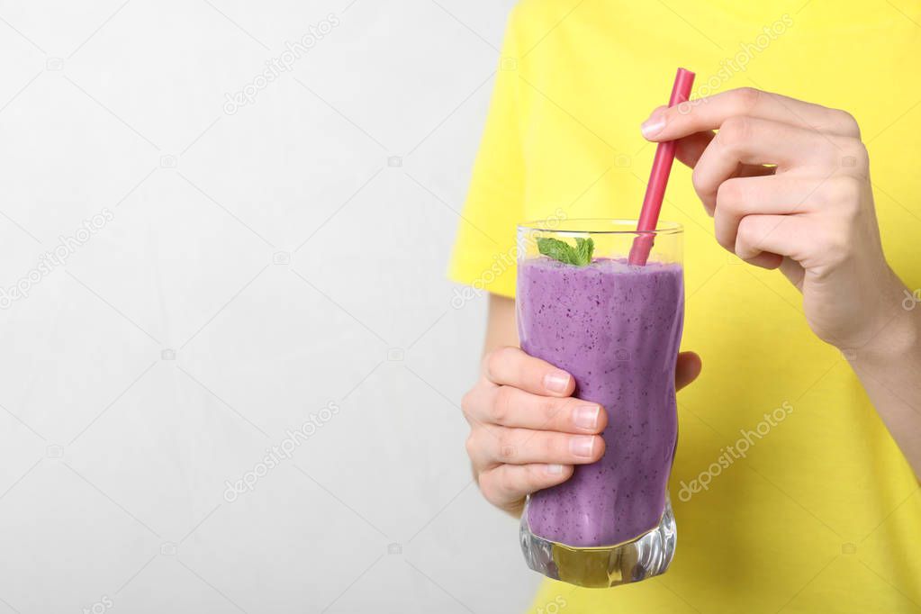Woman holding glass of delicious blueberry smoothie on light background, closeup