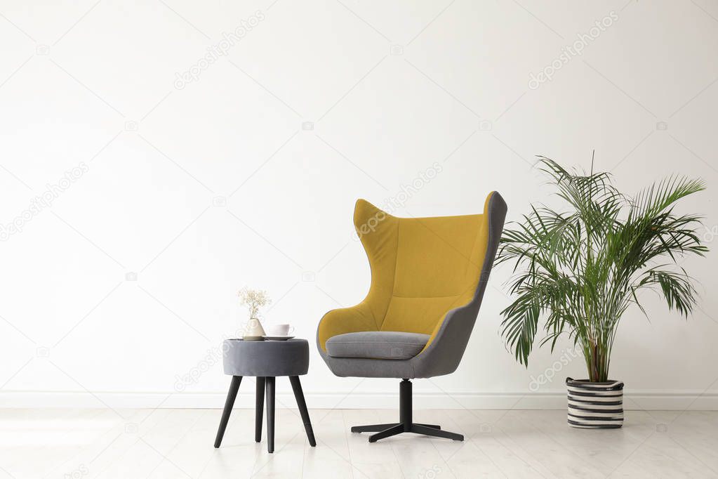 Stylish living room interior with comfortable armchair and houseplant near white wall. Space for text