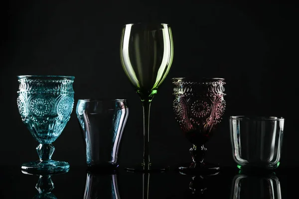 Ensemble de différents verres vides colorés sur fond noir — Photo