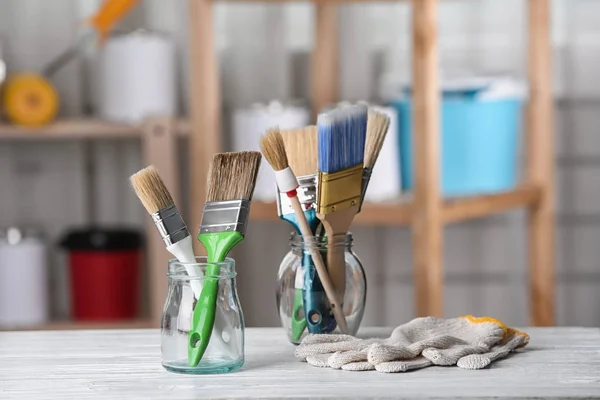 Glasgefäße mit Pinseln und Handschuhen auf Tisch in Werkstatt — Stockfoto