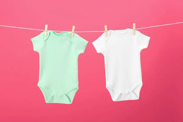 Bebê onesies pendurado na linha de roupas contra fundo rosa — Fotografia de Stock