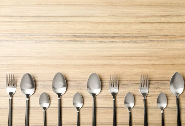 Nuevas horquillas y cucharas sobre mesa de madera, plano con espacio para el texto —  Fotos de Stock