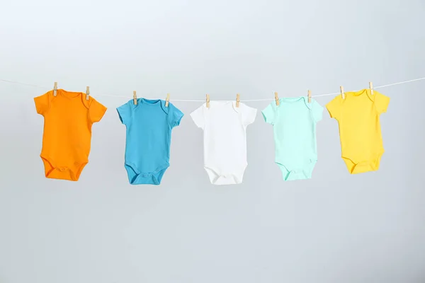 Різні дитячі онезії висять на лінії одягу на світло-сірому тлі. День прання — стокове фото