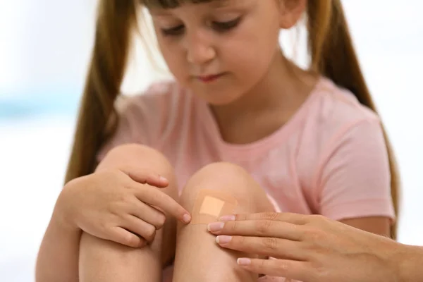 Woman applying plaster on girl's knee, closeup view