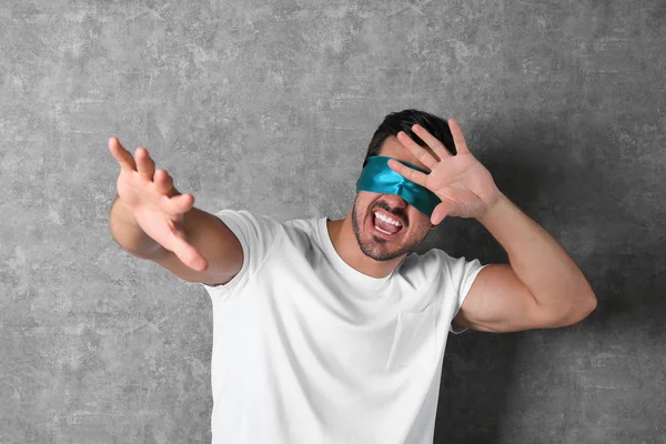 Young man wearing light blue blindfold on grey background — Stock Photo, Image