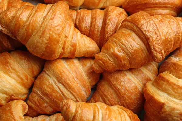 Friss ízletes croissant, mint a háttér, closeup. Francia cukrászsütemény — Stock Fotó