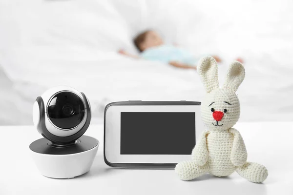 Babyfon, Kamera und Spielzeug auf dem Tisch neben dem Bett mit Kind im Zimmer. Video-Kindermädchen — Stockfoto