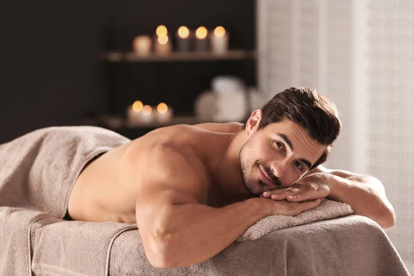 Bonito jovem relaxante na mesa de massagem no salão de spa, espaço para texto — Fotografia de Stock