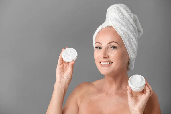 Retrato de una hermosa mujer madura con una piel perfecta sosteniendo frascos de crema sobre fondo gris —  Fotos de Stock