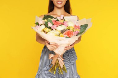 Genç kadın sarı arka plan üzerinde güzel çiçek buketi tutan, closeup