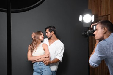 Profesyonel fotoğrafçı modern stüdyoda koyu gri arka plan üzerinde genç çiftin fotoğrafını çekiyor