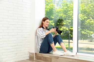 Pencerenin yakınında oturan modern kamera ile profesyonel fotoğrafçı kapalı