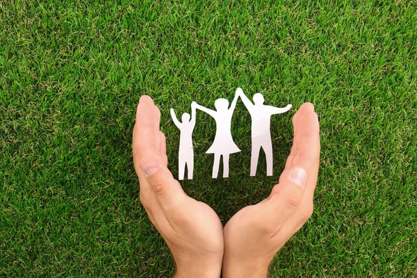 Man holding hands near paper silhouette of family on green grass, top view