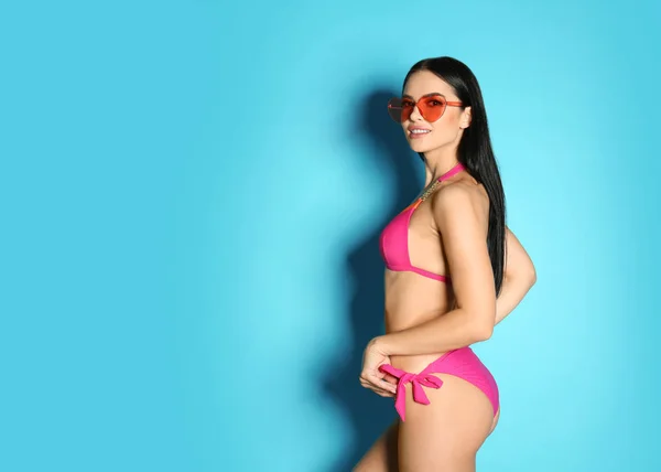Bella giovane donna in bikini elegante con occhiali da sole su sfondo azzurro. Spazio per testo — Foto Stock