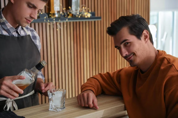 Bartender derramando uísque para o cliente no balcão no pub — Fotografia de Stock
