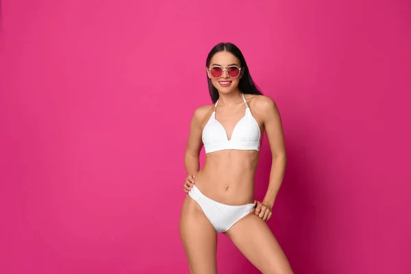 Beautiful young woman in white bikini with sunglasses on pink background. Space for text — Stock Photo, Image