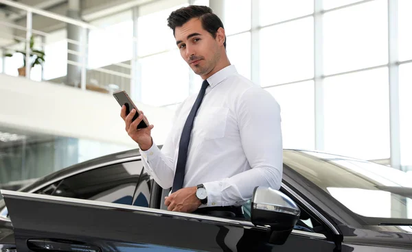 Jonge man met telefoon in de buurt van auto in modern dealer — Stockfoto