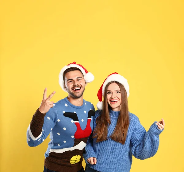 Coppia che indossa maglioni di Natale e cappelli di Babbo Natale su sfondo giallo — Foto Stock