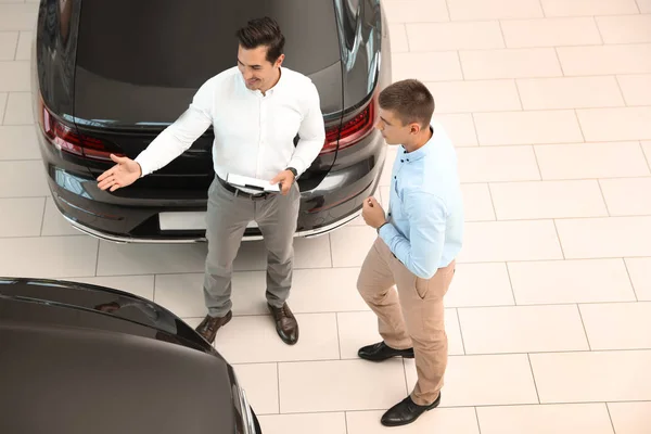 Jonge verkoper die samenwerkt met de klant in de moderne autodealer, boven de weergave — Stockfoto
