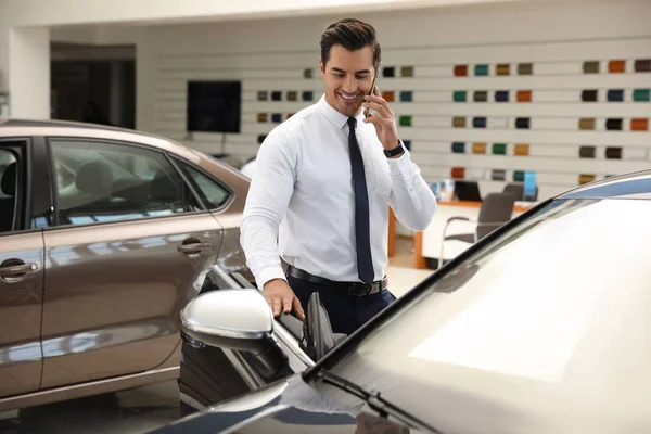Młody człowiek rozmawia na telefon w pobliżu samochodu w nowoczesnym salonie — Zdjęcie stockowe