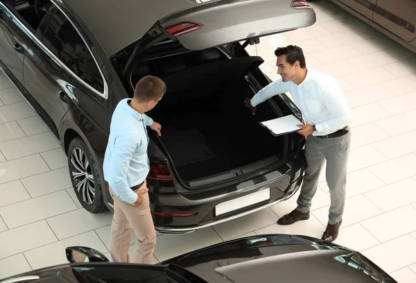 Jonge verkoper die samenwerkt met de klant in de moderne autodealer, boven de weergave — Stockfoto