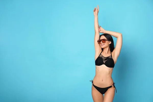Bella giovane donna in bikini elegante con occhiali da sole su sfondo azzurro. Spazio per testo — Foto Stock
