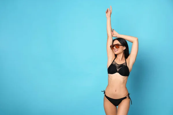 Hermosa mujer joven en bikini elegante con gafas de sol sobre fondo azul claro. Espacio para texto —  Fotos de Stock