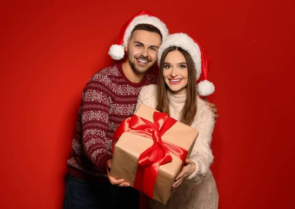 Pár karácsonyi pulóverek és Santa kalap díszdobozban piros háttér — Stock Fotó